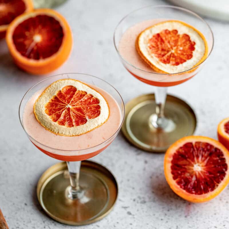 Two glasses of blood orange amaretto sour with oranges around them.
