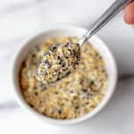 A spoonful of everything bagel seasoning being lifted up over the bowl.
