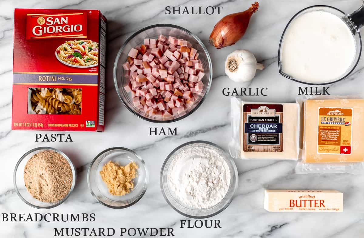 Ingredients needed to make a ham and cheese casserole on a marble background with text overlay.