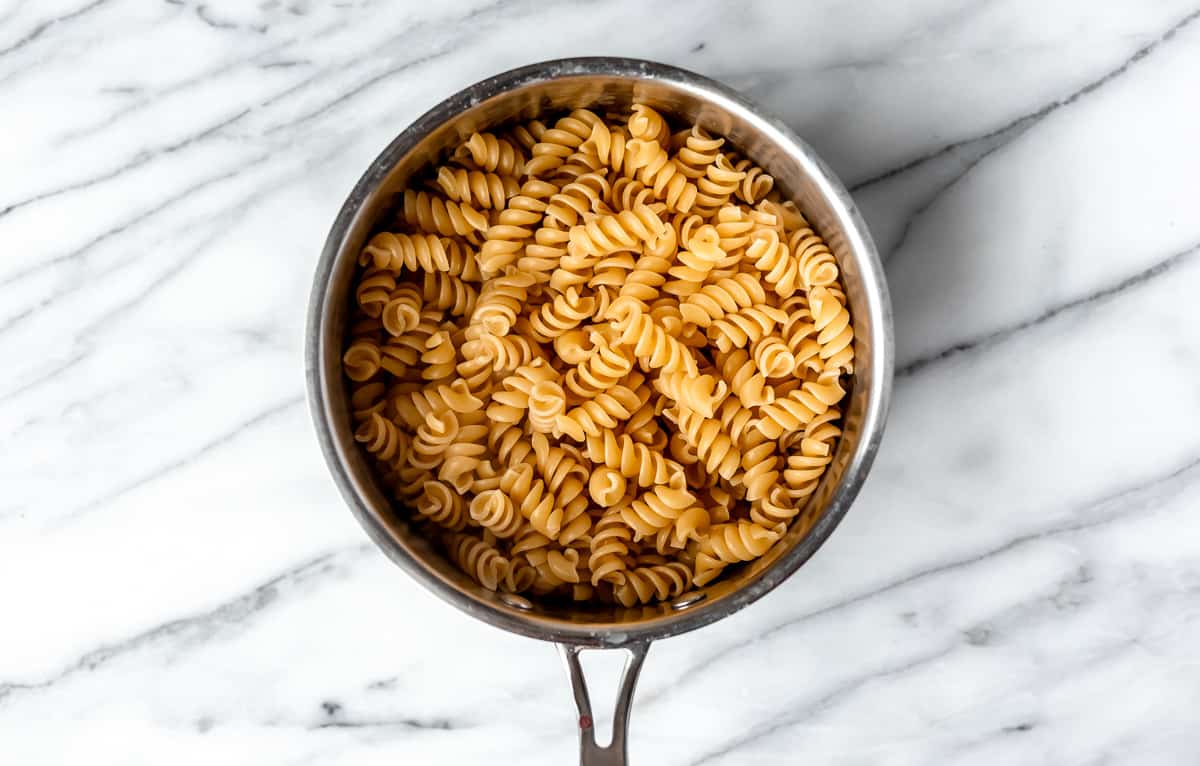 Rotini pasta in a silver pot over a marble background.