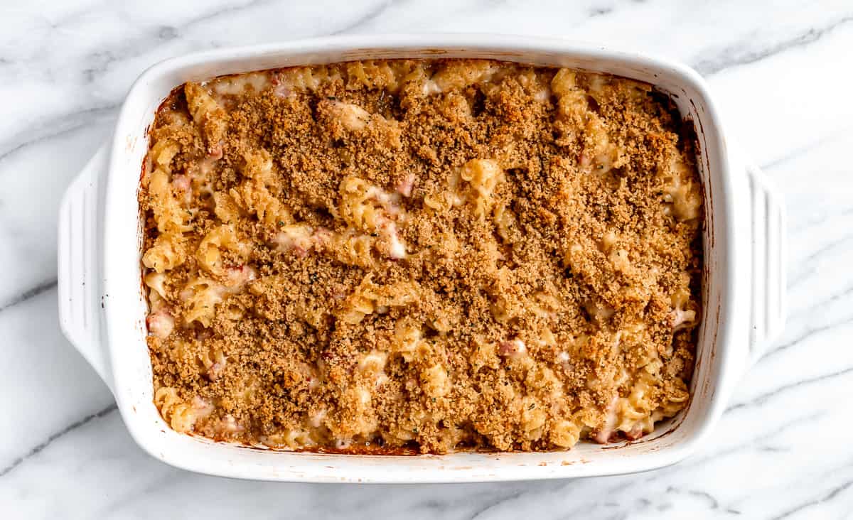A baked ham and cheese casserole in a white, rectangular casserole dish over a marble background.