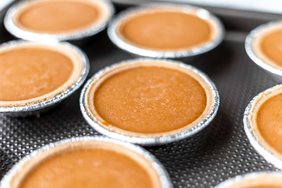 Close up of mini pie shells filled with pumpkin pie batter.