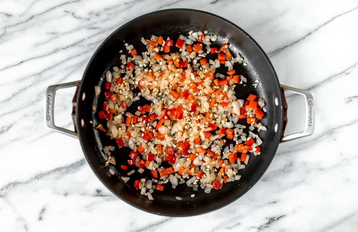 Diced red pepper, onion and garlic cooking in a black skillet.