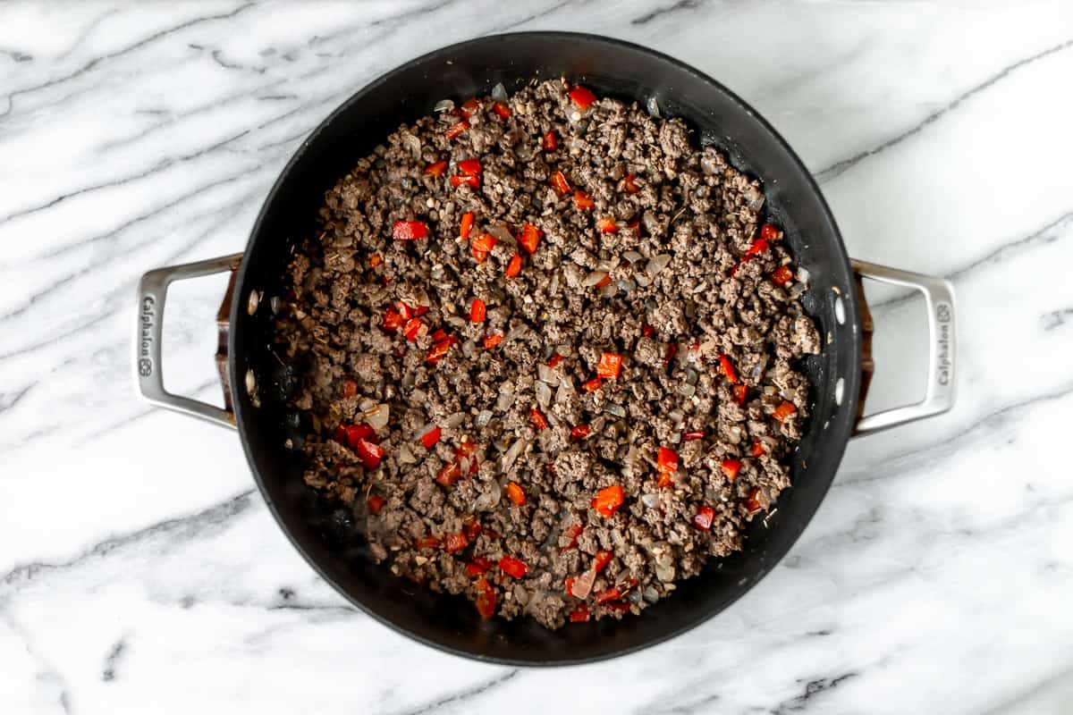 Ground beef, peppers, onion, and garlic cooking in a black skillet.