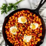 Overhead of sweet potato breakfast hash in a cast iron pan with parsley and a striped towel around it with text overlay.