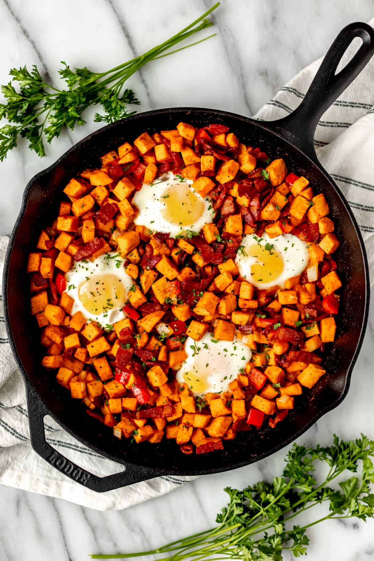 Overhead of sweet potato breakfast hash in a cast iron pan with parsley and a striped towel around it.