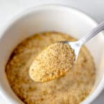 Adobo seasoning being held up on a small spoon over a white bowl of more seasoning with text overlay.
