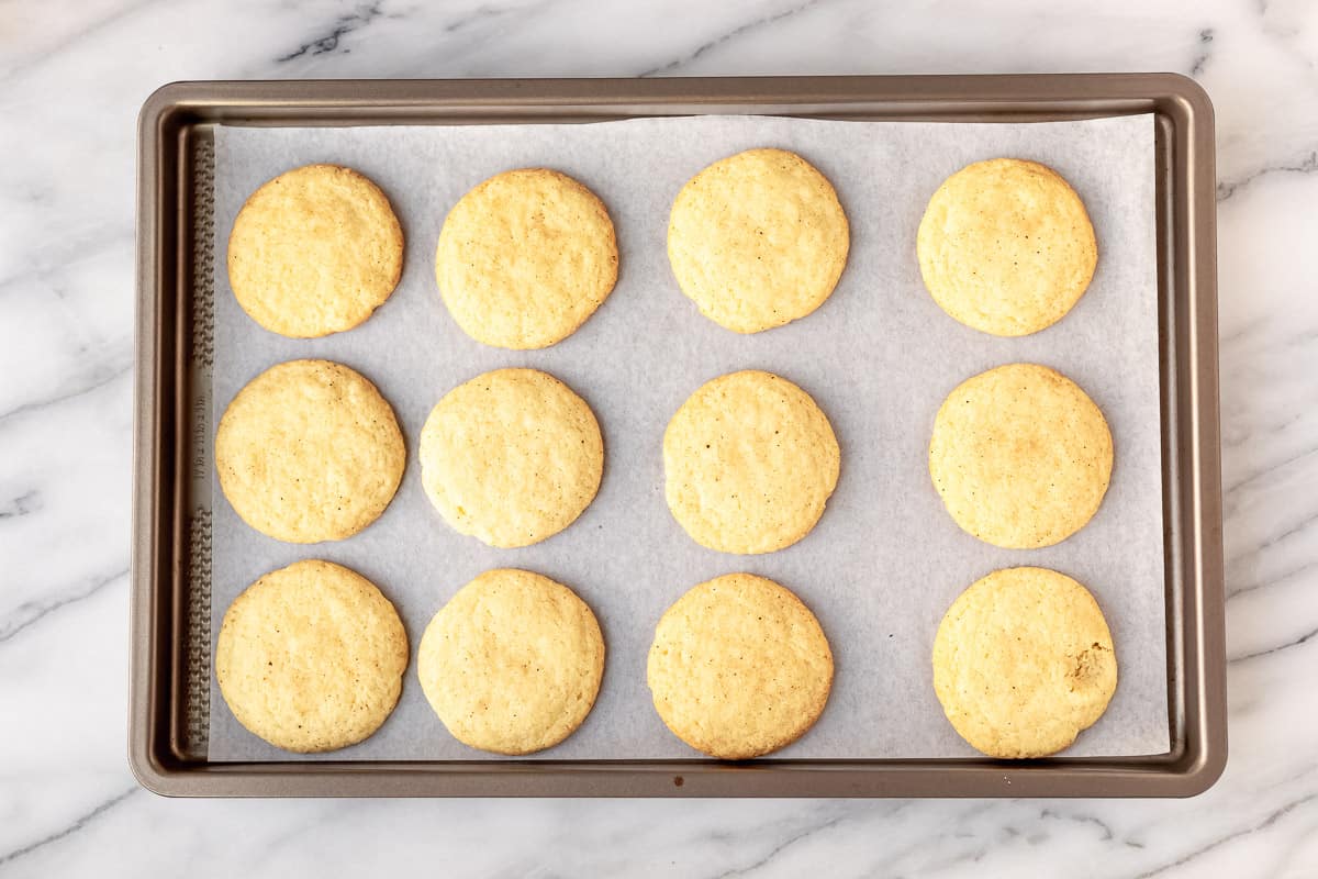 Twelve baked chai spice snickerdoodles on a parchment paper lined baking sheets.
