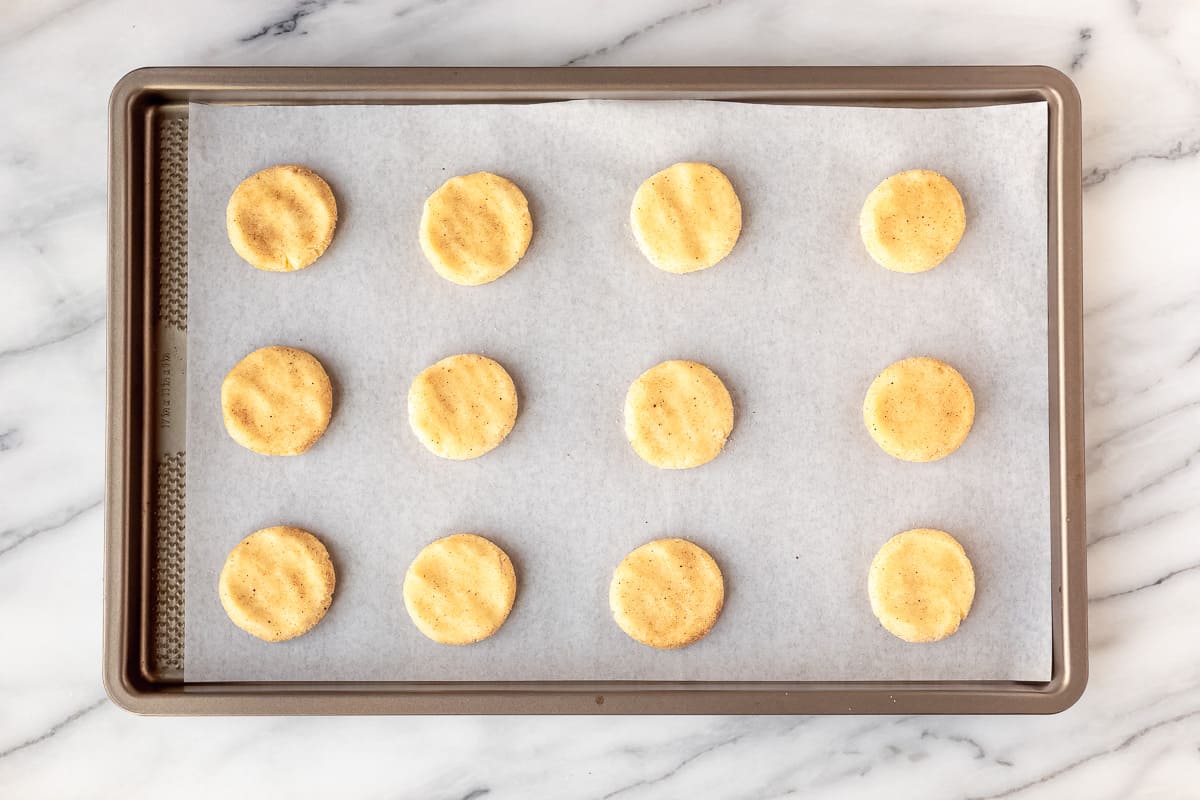 Flattened snickerdoodle dough balls on a parchment paper lined baking sheet.