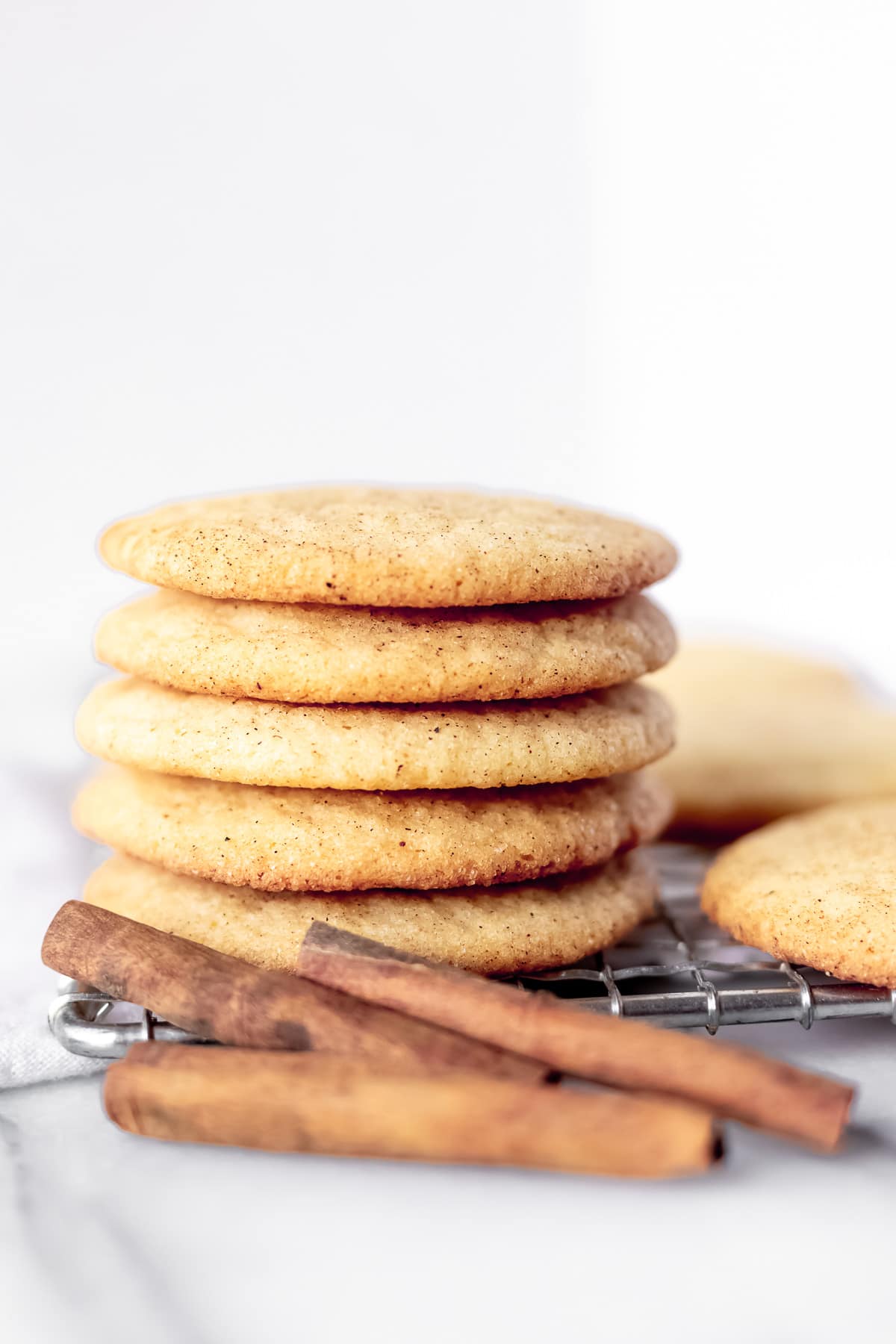 A stack if chai spice snickerdoodle cookies with 3 cinnamon sticks in front of them.