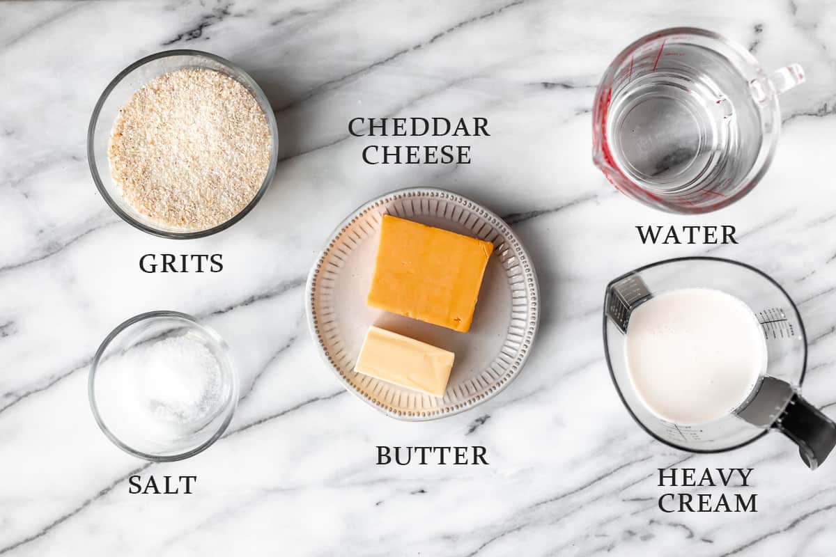 Ingredients to make cheddar cheese grits on a marble background with text overlay.