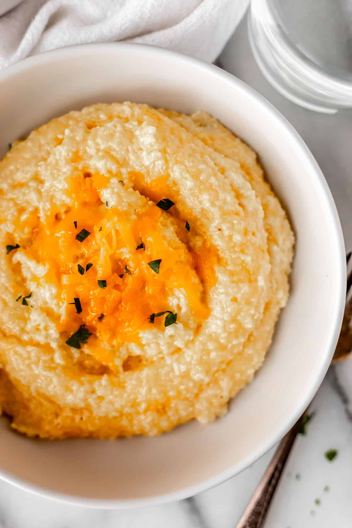 Close up overhead of a white bowl filled with cheddar cheese grits and garnished with cheese and minced parsley.