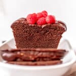 A chocolate pound cake with two slices laying in front of the remaining cake on a white serving plate. The cake is topped with fresh raspberries.
