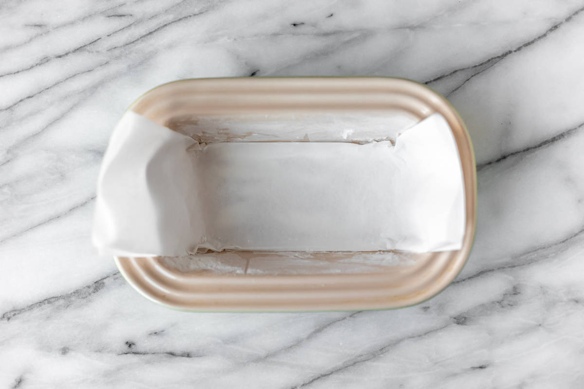 Overhead of a loaf pan with parchment paper inside on a marble background.