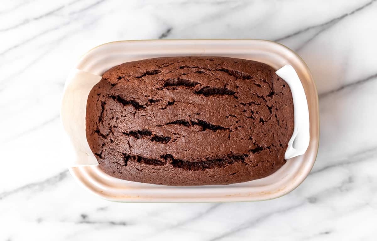A baked chocolate pound cake in a loaf pan on a marble background.