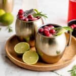 Two Cranberry Moscow Mules in copper mugs on a wood serving tray.