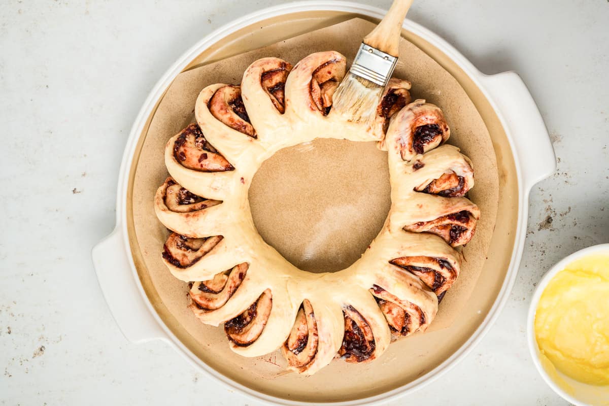 An unbaked cinnamon roll wreath being brushed with butter.