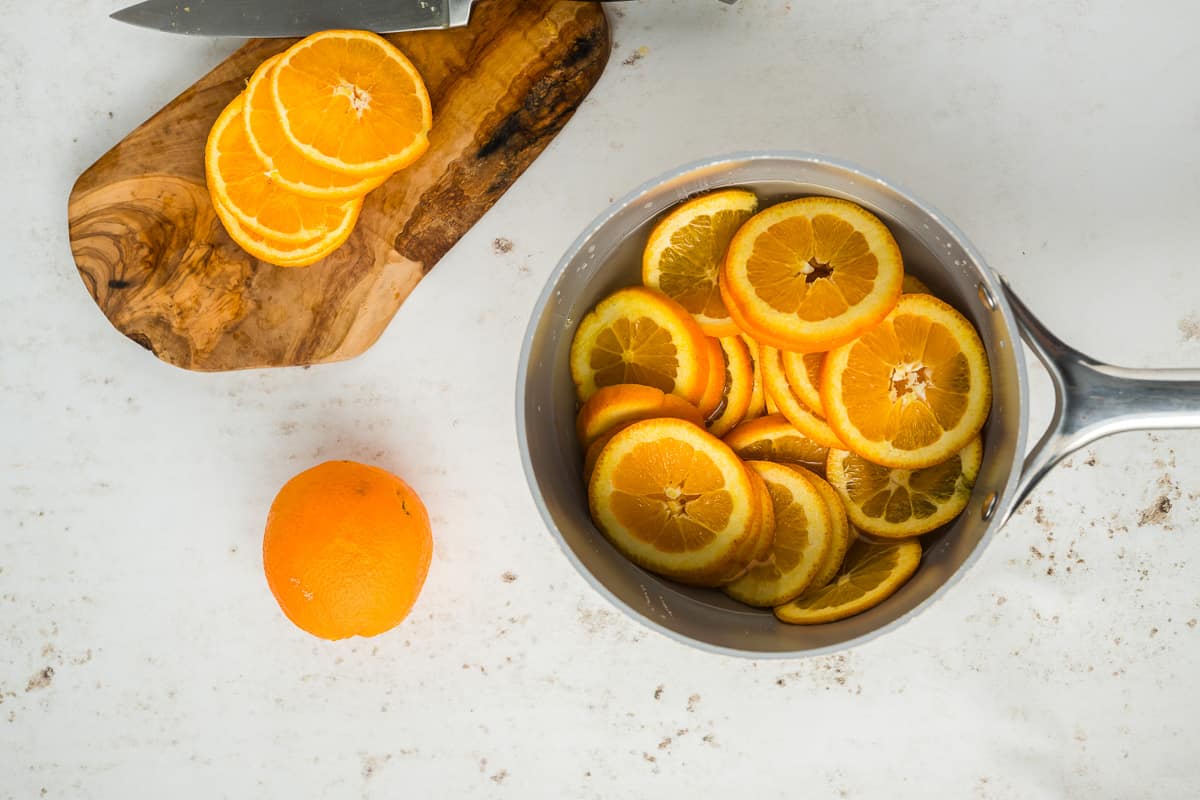 Slices of oranges in a pot with more orange slices in a cutting board with a knife.