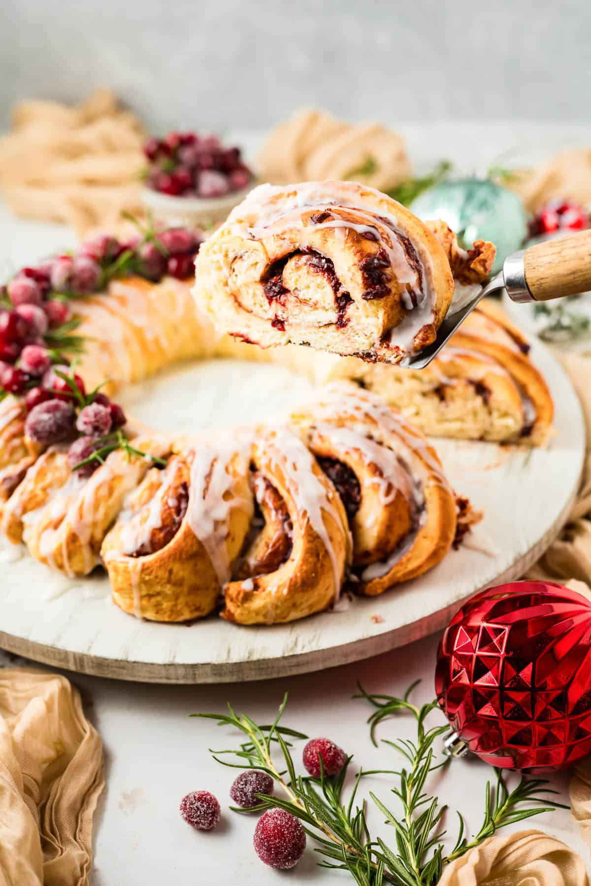A serving of Orange Cranberry Cinnamon Roll Wreath being lifted up on a server over the remaining wreath.
