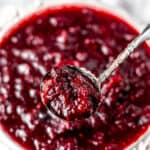 Cranberry sauce on a spoon over a bowl of more cranberry sauce with text overlay.