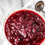 Cranberry sauce in a white bowl with a silver spoon and text overlay.