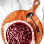Cranberry sauce in a white bowl on a wood server with a silver spoon and text overlay.