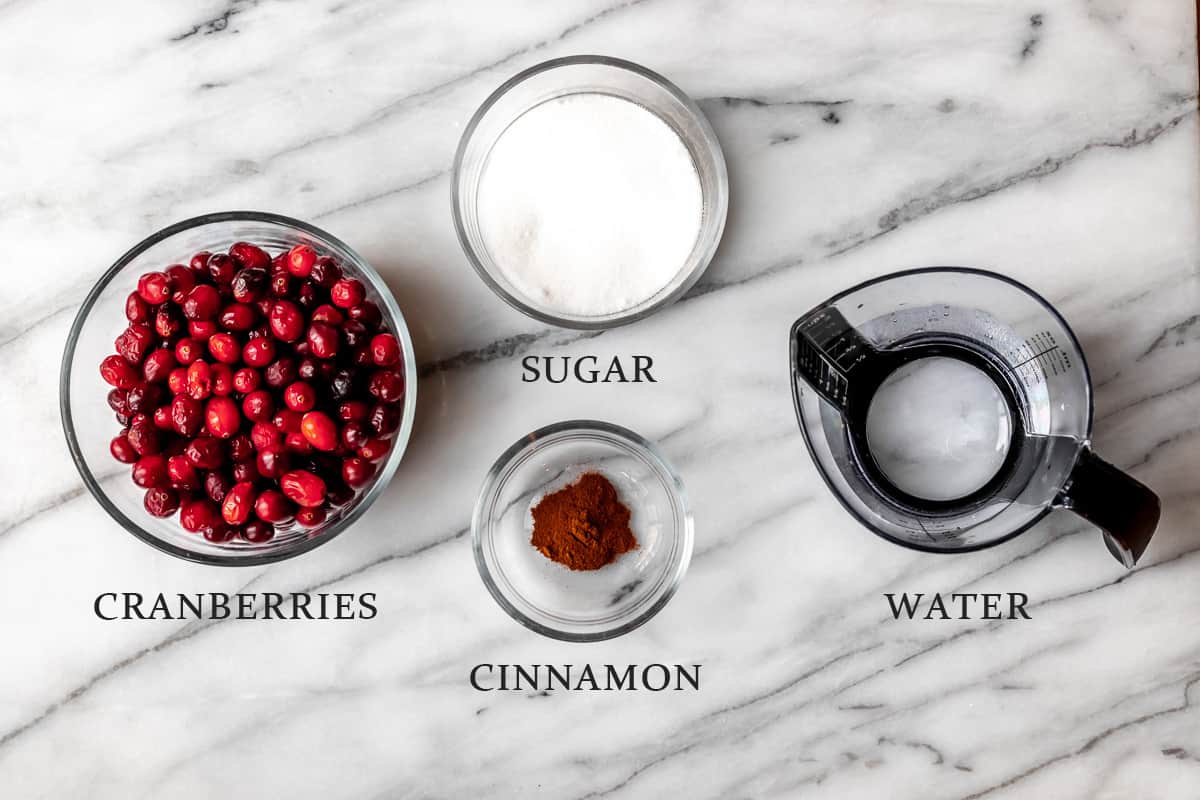Ingredients needed to make cranberry sauce on a marble background with text overlay.