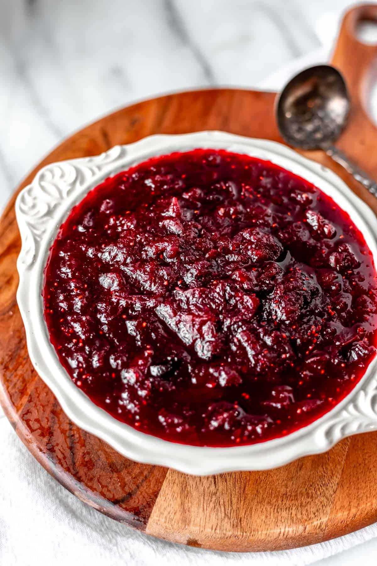 A bowl of cranberry sauce on a wood server with a silver spoon.
