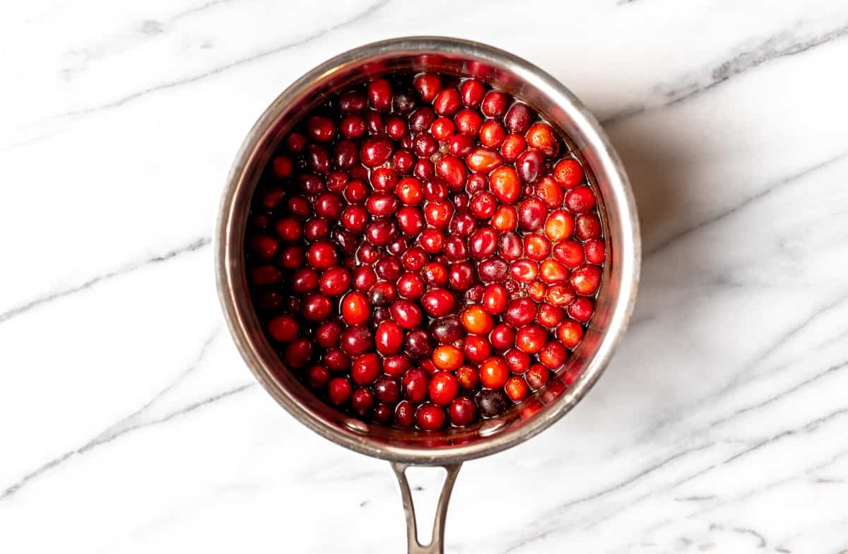 Cranberries in a silver sauce pan over a marble background.