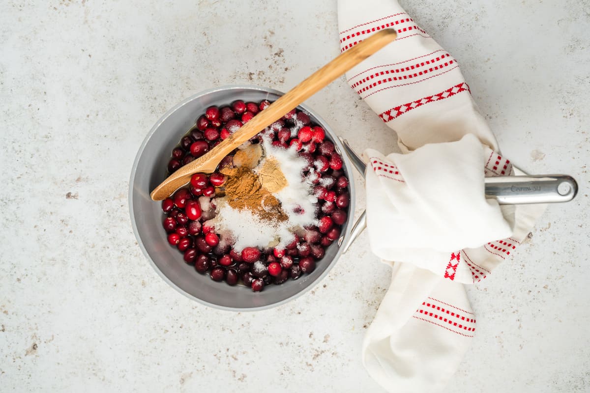 Cranberries, sugars, and spices in a pot with a spoon in it.