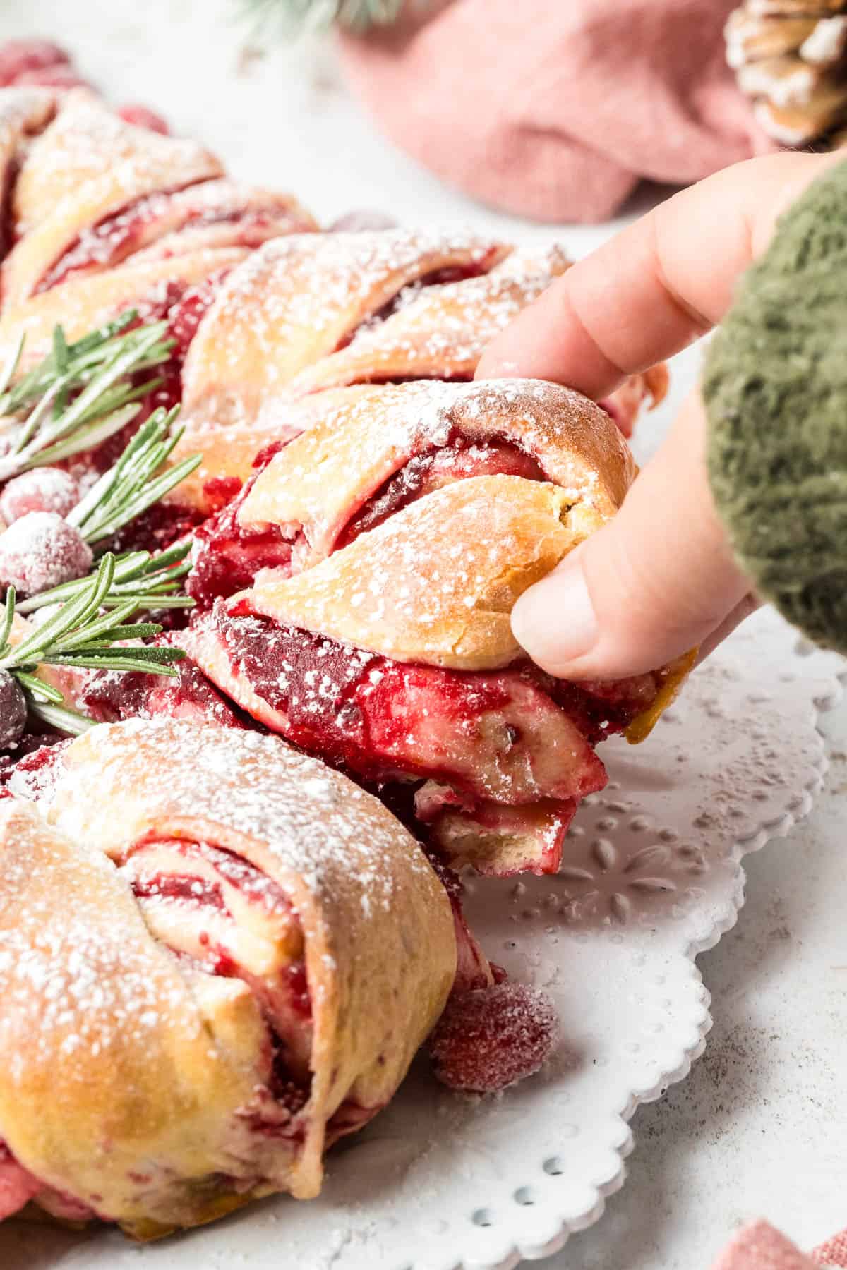 A hand taking a piece of cranberry star bread.