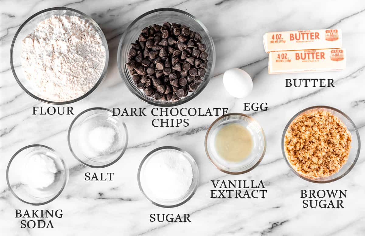 Ingredients needed to make dark chocolate chip cookies on a marble background with text overlay.