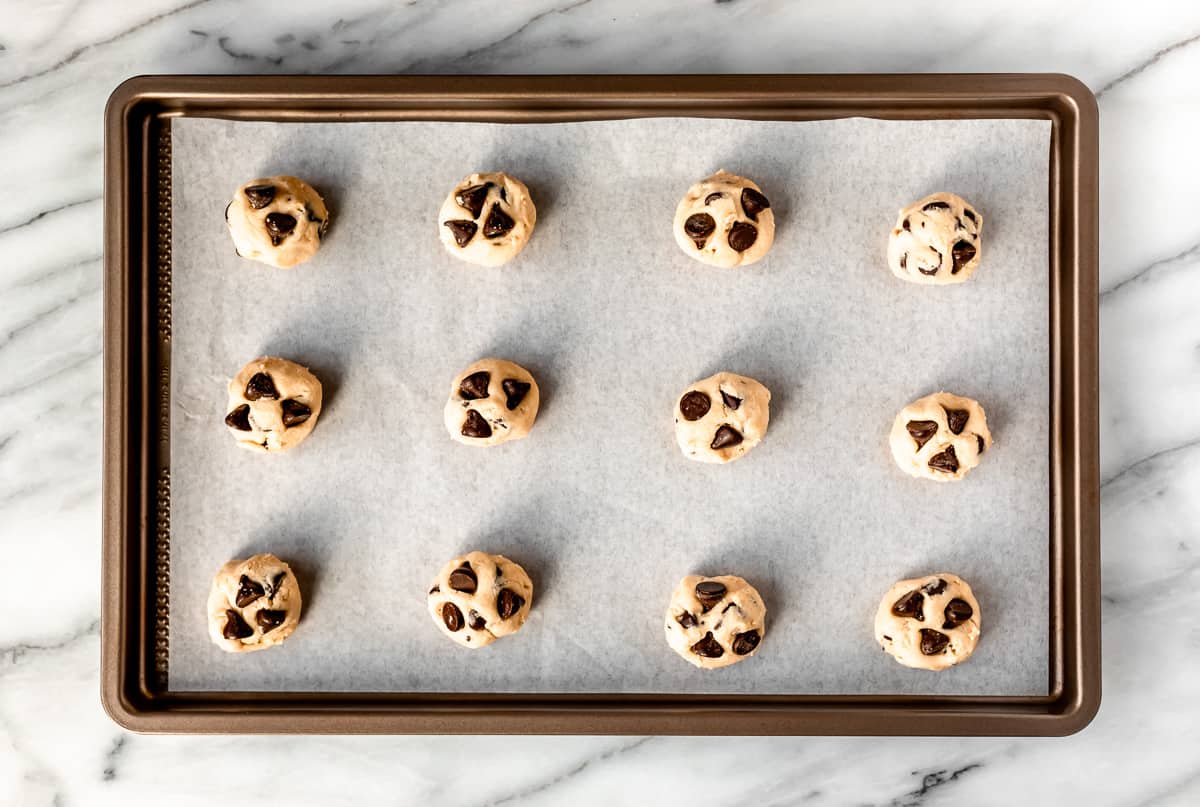 Twelve cookie dough balls on a parchment paper lined baking sheet.