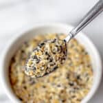 Everything bagel seasoning in a small white bowl with a spoon lifting some up and text overlay.