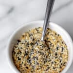 Everything bagel seasoning in a small white bowl with a spoon in it and text overlay.