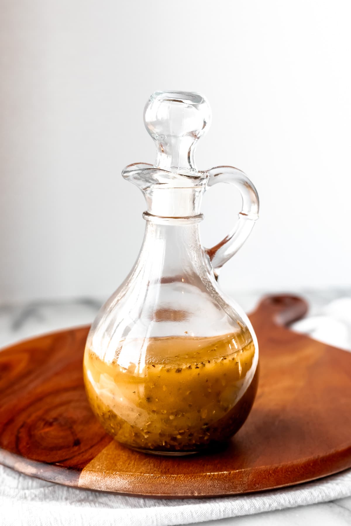 Greek Salad Dressing in a glass cruet on a wood turner with a white background.