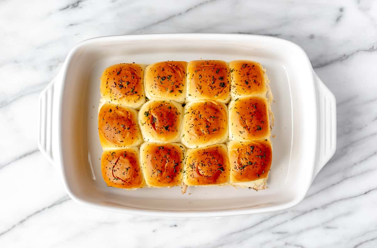 Overhead of baked turkey sliders in a white casserole dish.