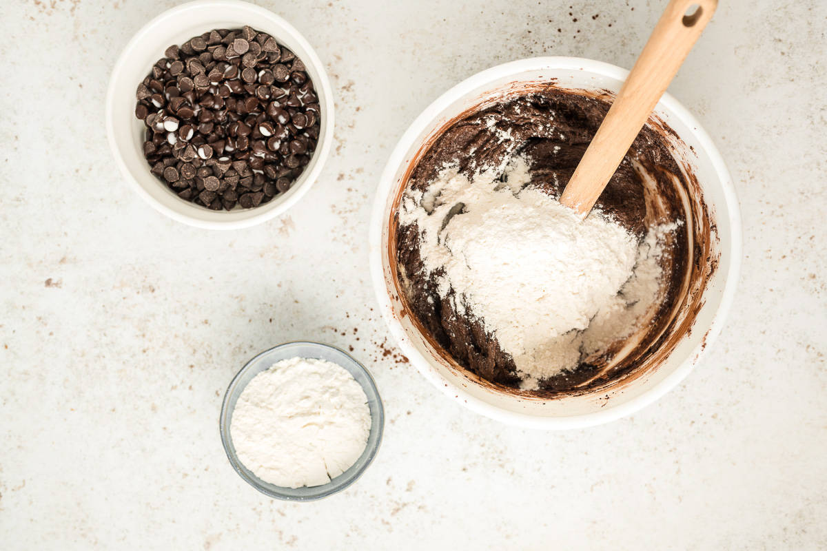 A bowl of brownie batter with flour in it and other ingredients around it.