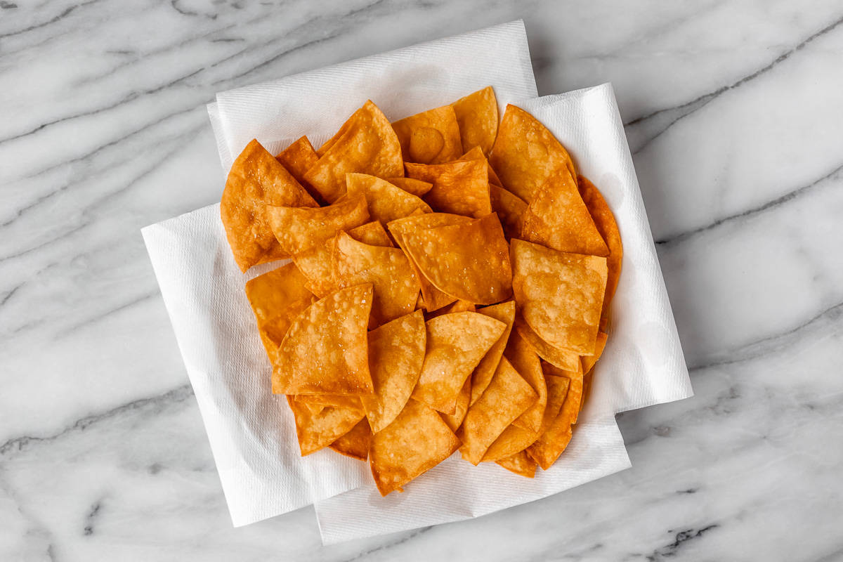 Fried corn tortilla chips on a paper towel lined plate over a marble table.