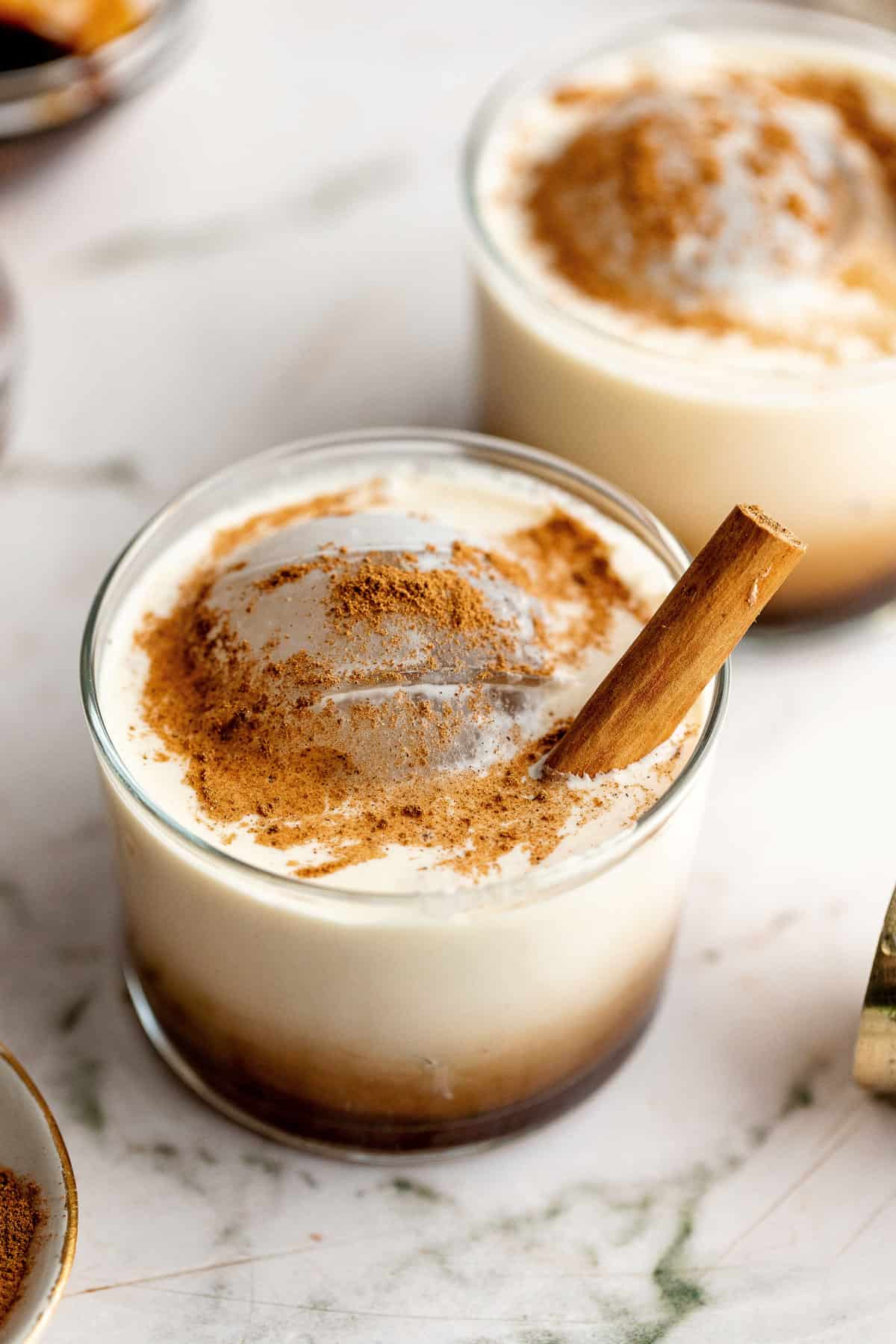 Two Gingerbread White Russian cocktails with cinnamon sticks in it on a white background.