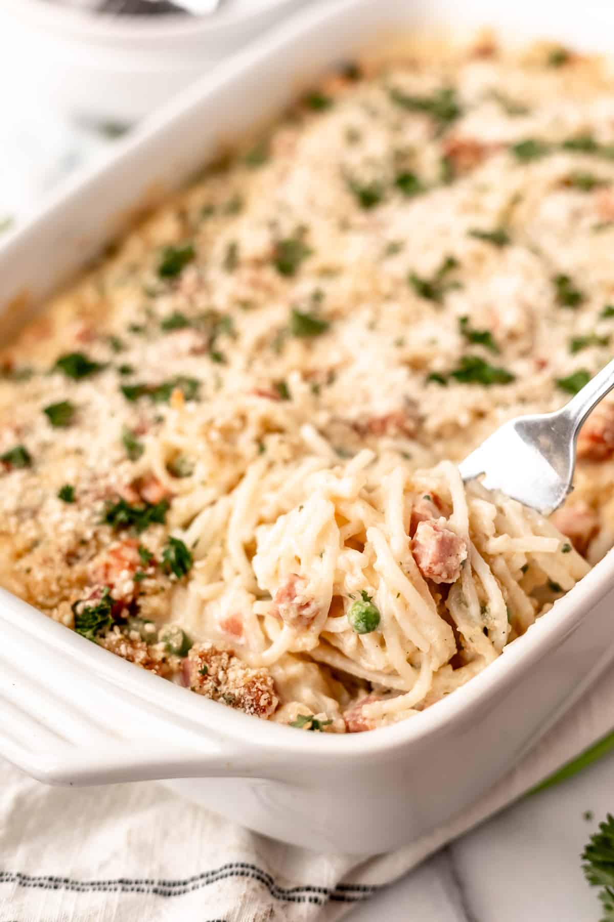 Ham tetrazzini in a white casserole dish with some being lifted up with fork.