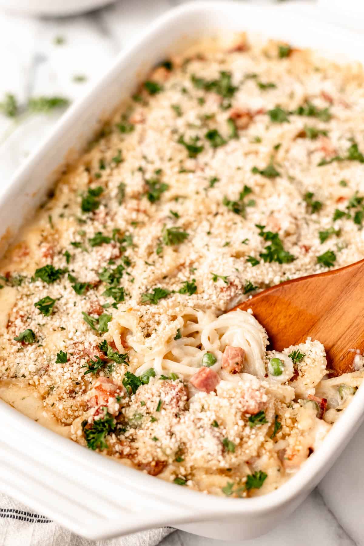 Close up of ham tetrazzini in a white casserole dish with some being pushed up with a wood turner.