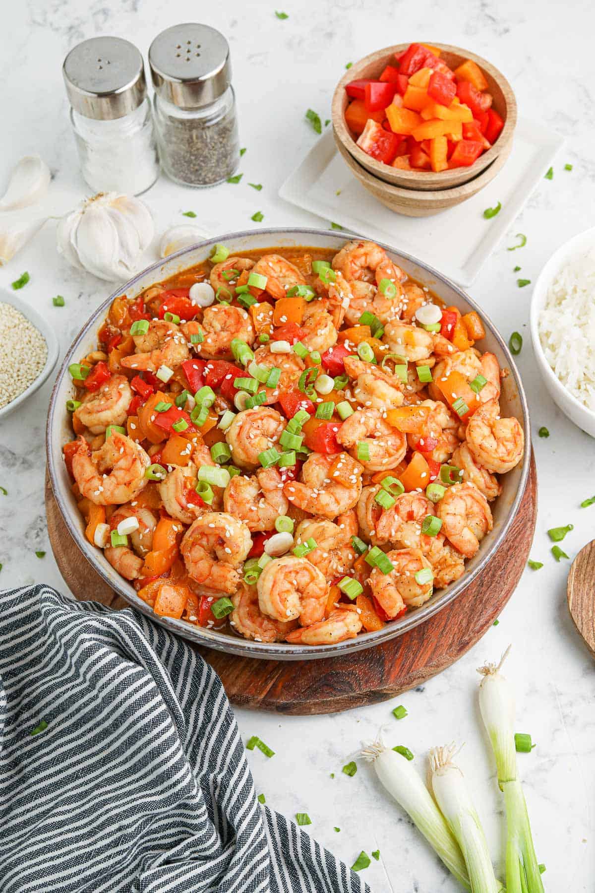 A large bowl of Kung Pao Shrimp surrounded by other ingredients and a striped towel.