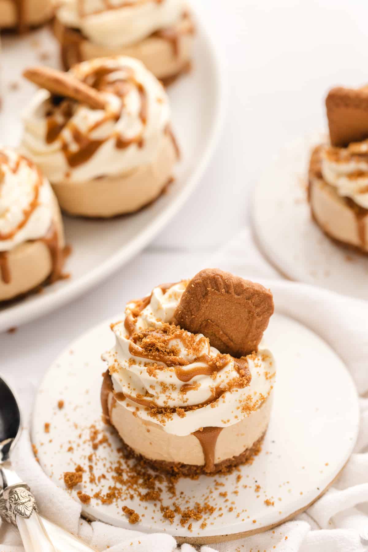 Mini Biscoff Cheesecakes on white plates with a serving try of more cheesecake in the background.
