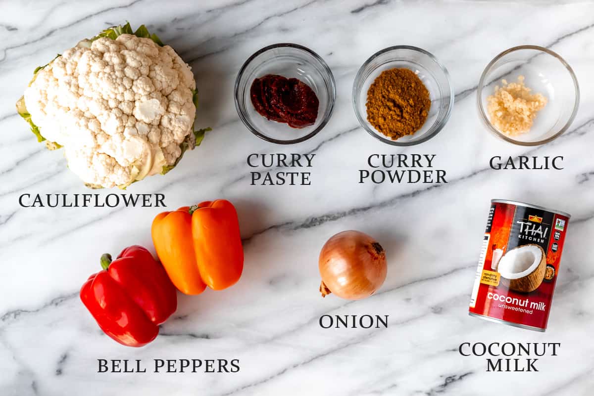 Ingredients needed to make Roasted Cauliflower Curry on a marble surface with text overlay.