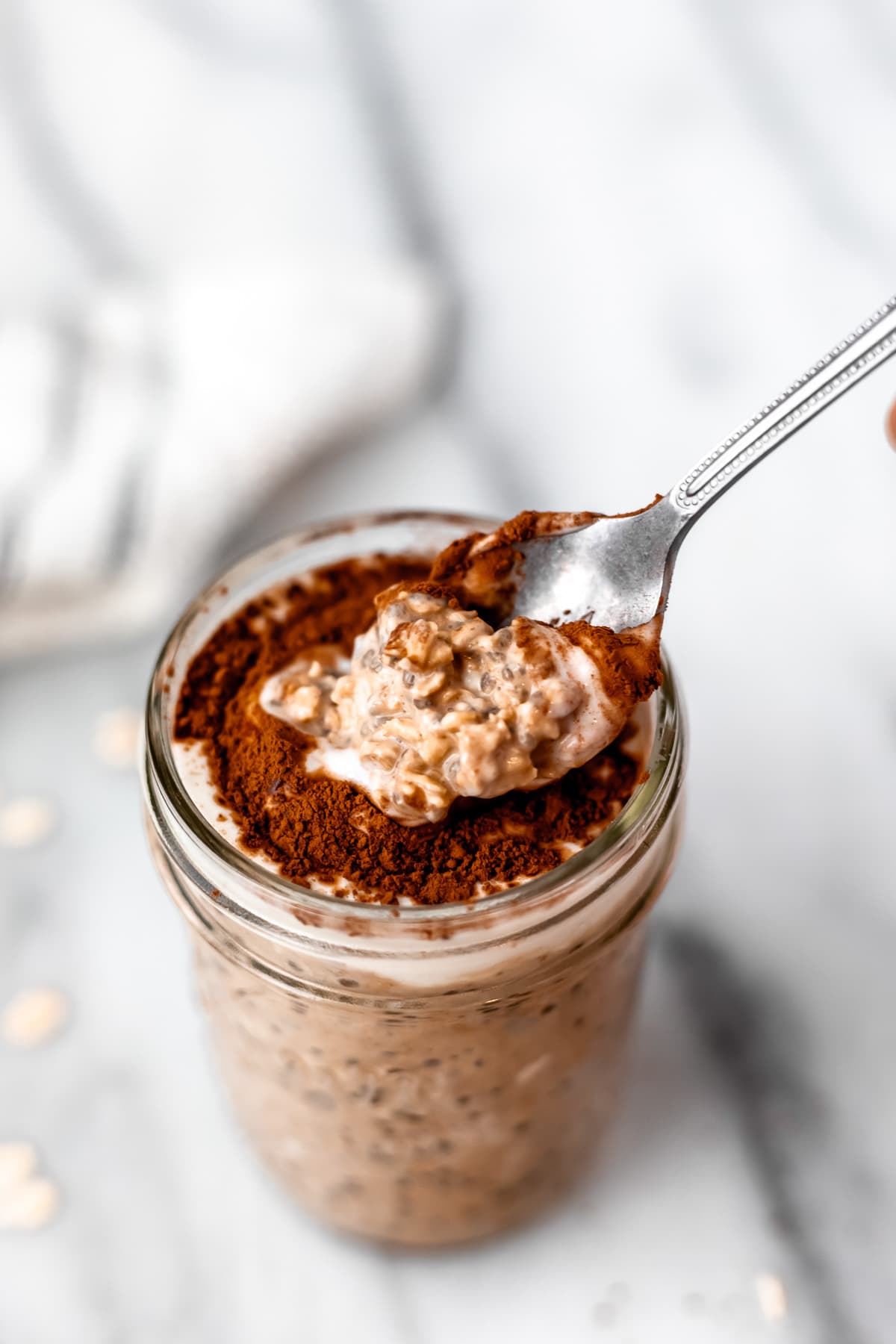 A mason jar filled with tiramisu overnight oats with a spoon lifting up some of the oatmeal.