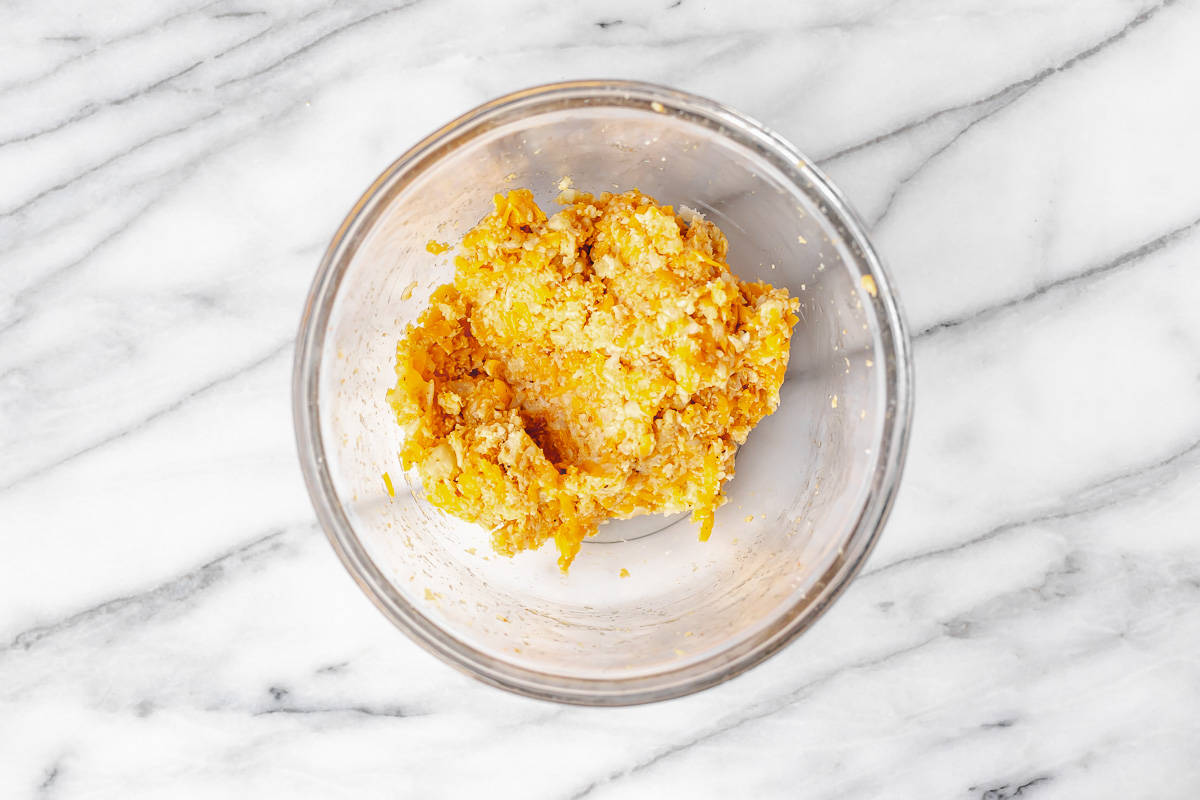 Cauliflower hash brown dough in a glass bowl over a marble background.