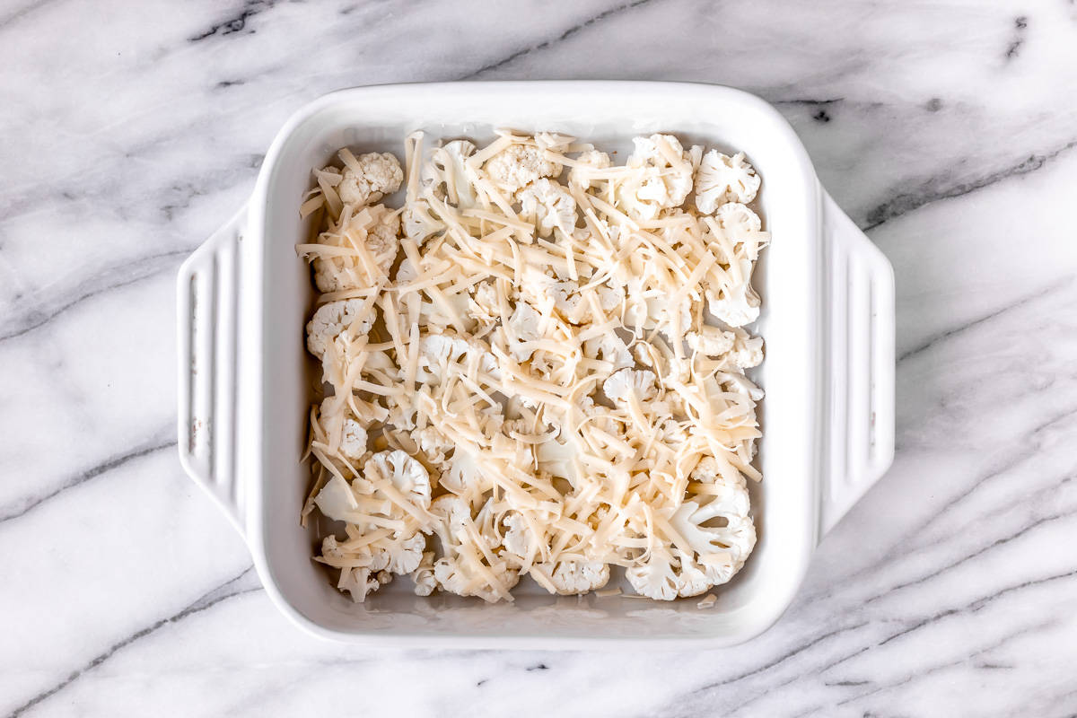 Slices of cauliflower topped with shredded cheese in a white, square baking dish.