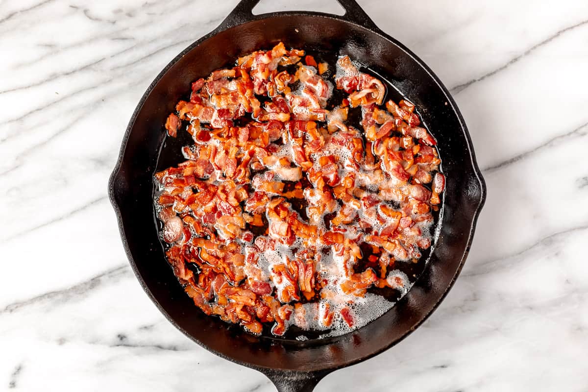 Diced bacon cooking in a black skillet.