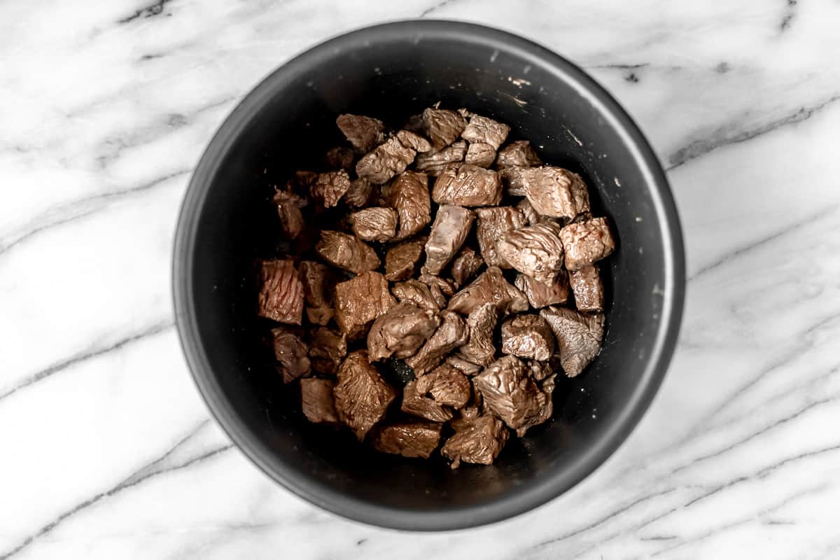 Cooked beef cubes in the bottom on an Instant Pot.